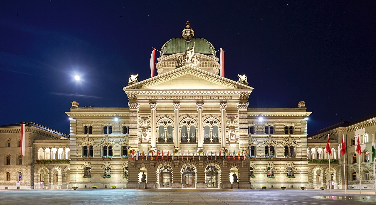 Federal Palace of Switzerland with full flags due to Indian President's state visit. Plaza view during full moon with clear night sky.
